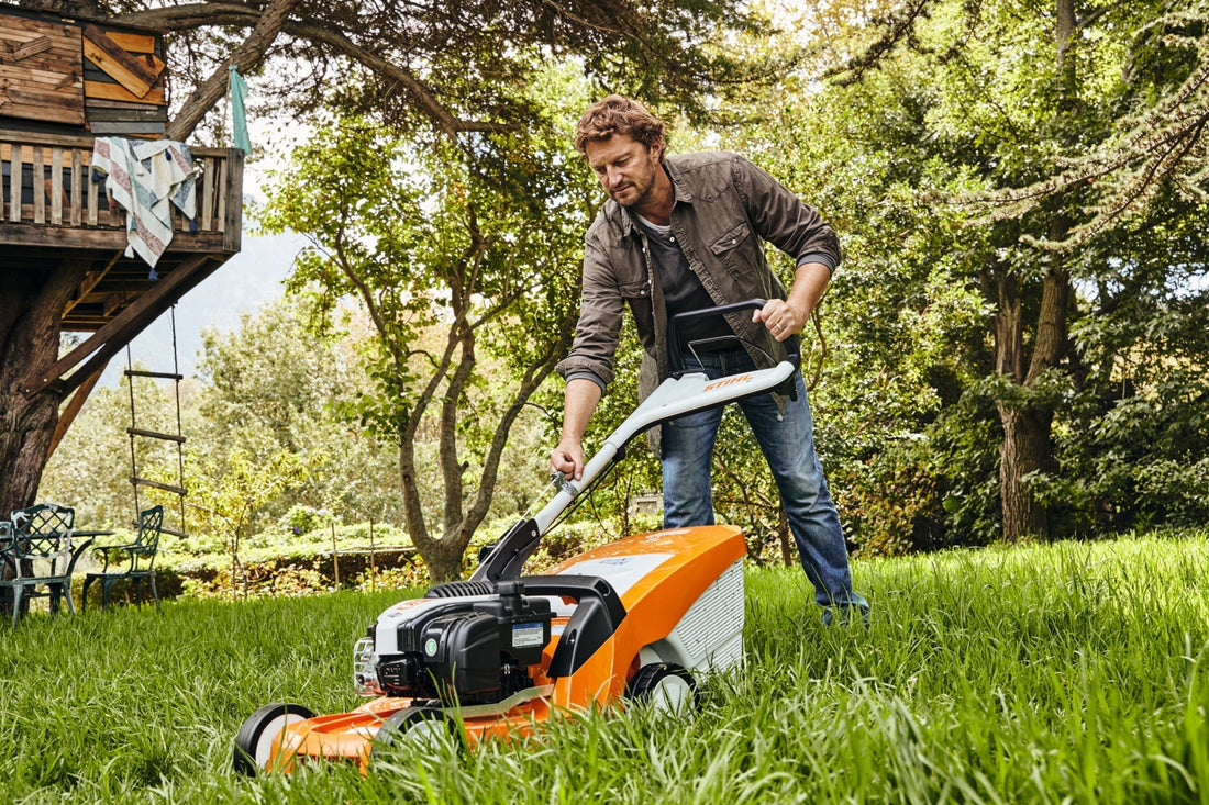 Ein Mann welcher einen STIHL Rasenmäher anmacht auf grünem Rasen