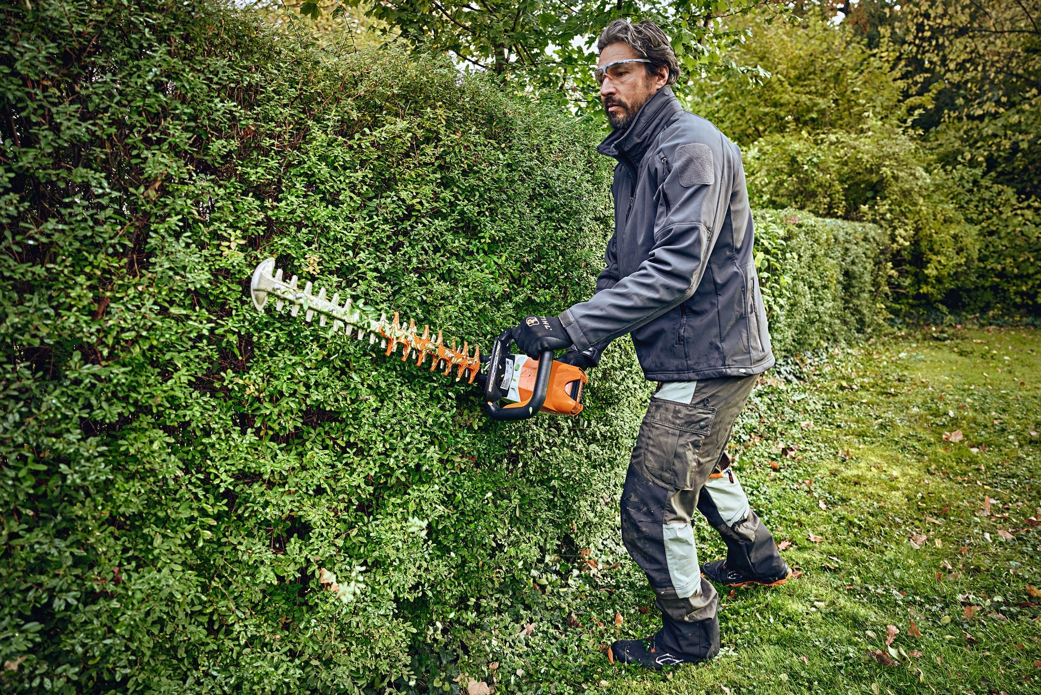 Ein Mann im mittleren Alter welcher eine STIHL Heckenschere an einer Hecke verwendet.
